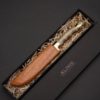 Μαχαίρι σκαφιδωτό με λάμα από ανοξείδωτο ατσάλι λαβή από ξανθό κέρατο κριού μπρούτζινο στήριγμα και μπρούτζινο κεφάλι κρητικού σε ξύλινη θήκη μέσα σε χάρτινη κασετίνα