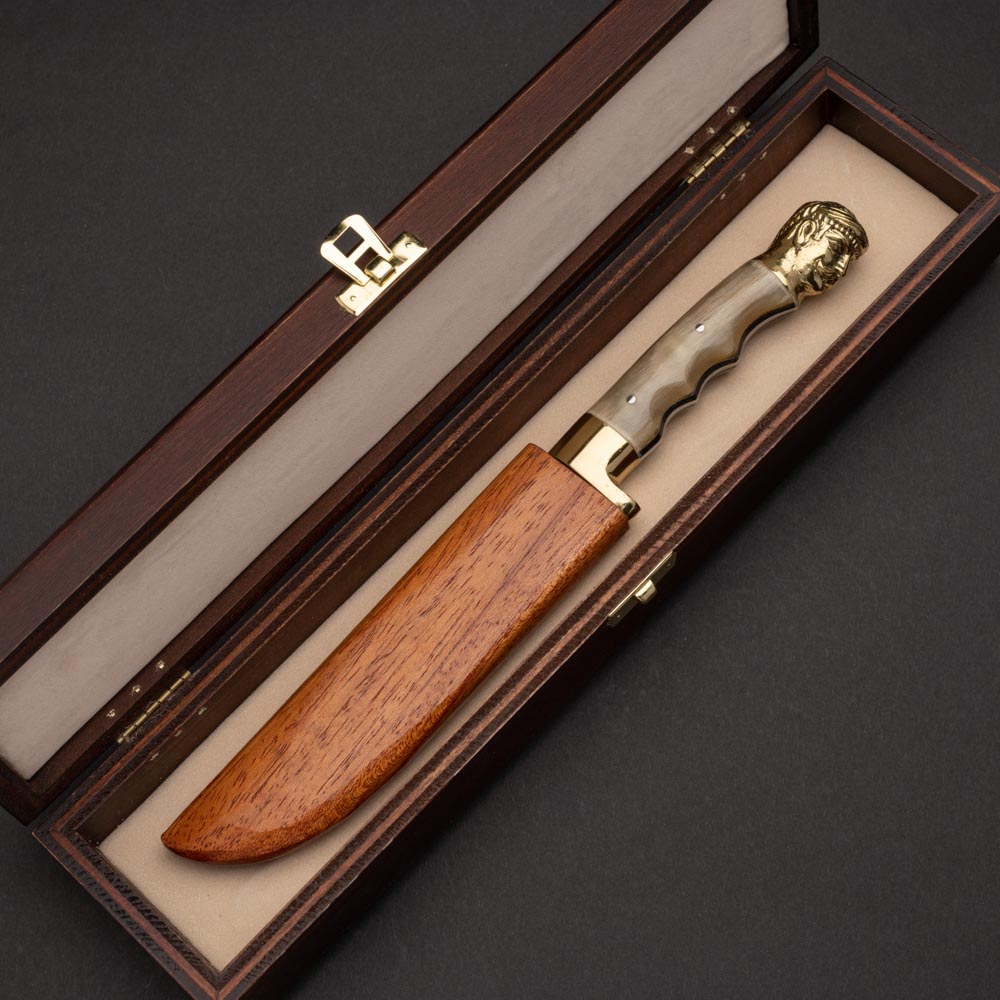 Μαχαίρι σκαφιδωτό με λάμα από ανοξείδωτο ατσάλι λαβή από ξανθό κέρατο κριού μπρούτζινο στήριγμα και μπρούτζινο κεφάλι κρητικού σε ξύλινη θήκη μέσα σε ξύλινη κασετίνα